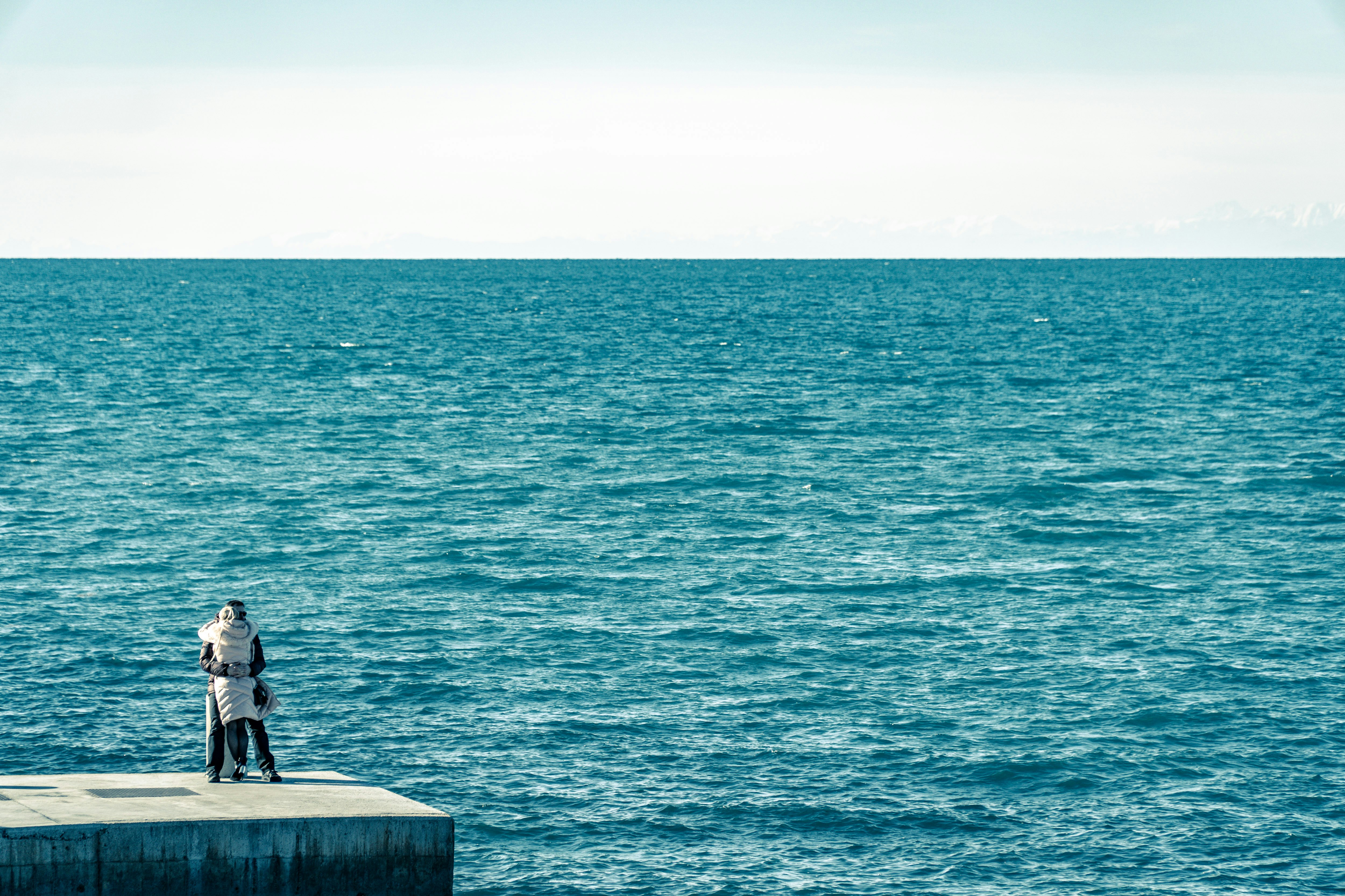 man in black jacket sitting on concrete bench near sea during daytime